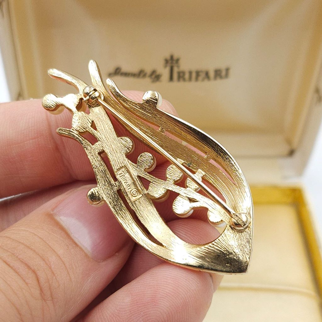 Spilla firmata Trifari risalente alla seconda metà degli anni cinquanta, realizzata in lega Trifanium color oro satinato con dettagli lucidi e perle - VINTAGE AMORE MIO Spilla firmata Trifari risalente alla seconda metà degli anni cinquanta, realizzata in lega Trifanium color oro satinato con dettagli lucidi e perle - VINTAGE AMORE MIO